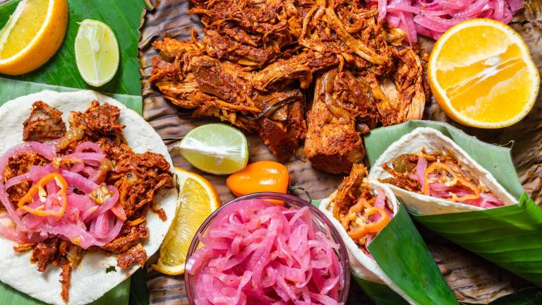 Cochinita Pibil, Mexican pit-roasted pork dish from Yucatan, on banana leaves with traditional condiments. Tacos and tostadas from Mexico.